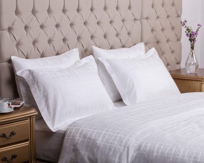Small golden tables on both sides of the white bed and four pillows leaning against the tufted headboard.